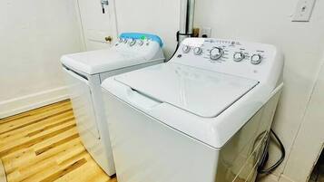 A laundry room with two white washing machines, a wooden floor, and a white door.