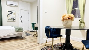 Una habitación con cama, una mesa con sillas, una ventana con cortinas y un aire acondicionado instalado en la pared.