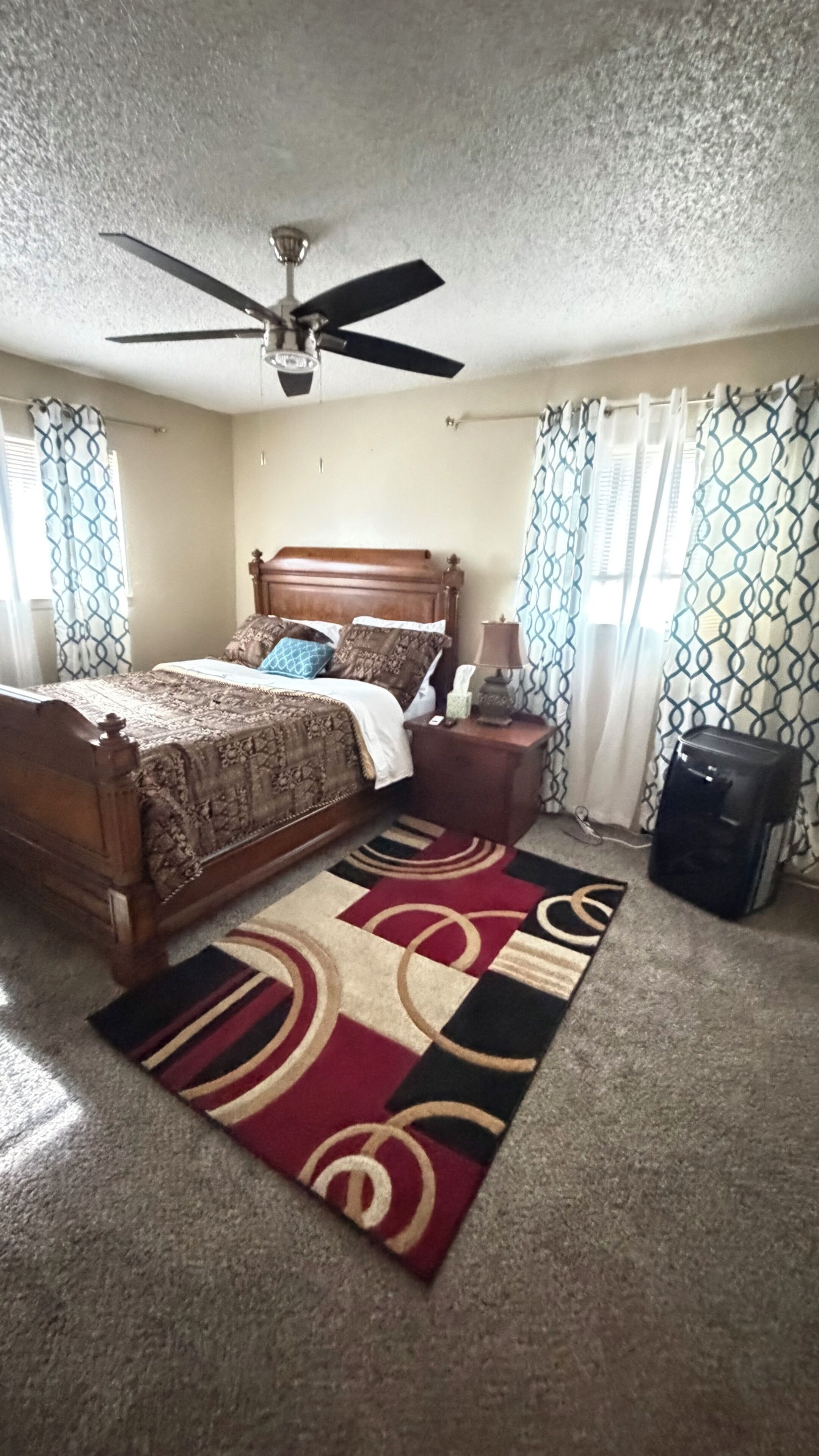 A bedroom with a bed, a nightstand, a lamp, a suitcase, and a ceiling fan.