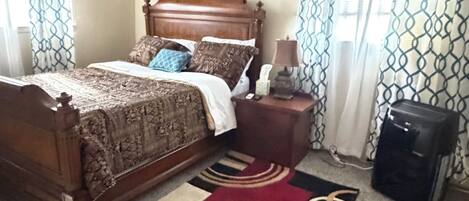 A bedroom with a bed, a nightstand, a lamp, a suitcase, and a ceiling fan.