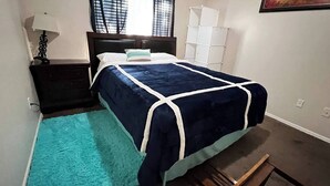 A bedroom with a bed, a nightstand, a lamp, and a window with blinds.