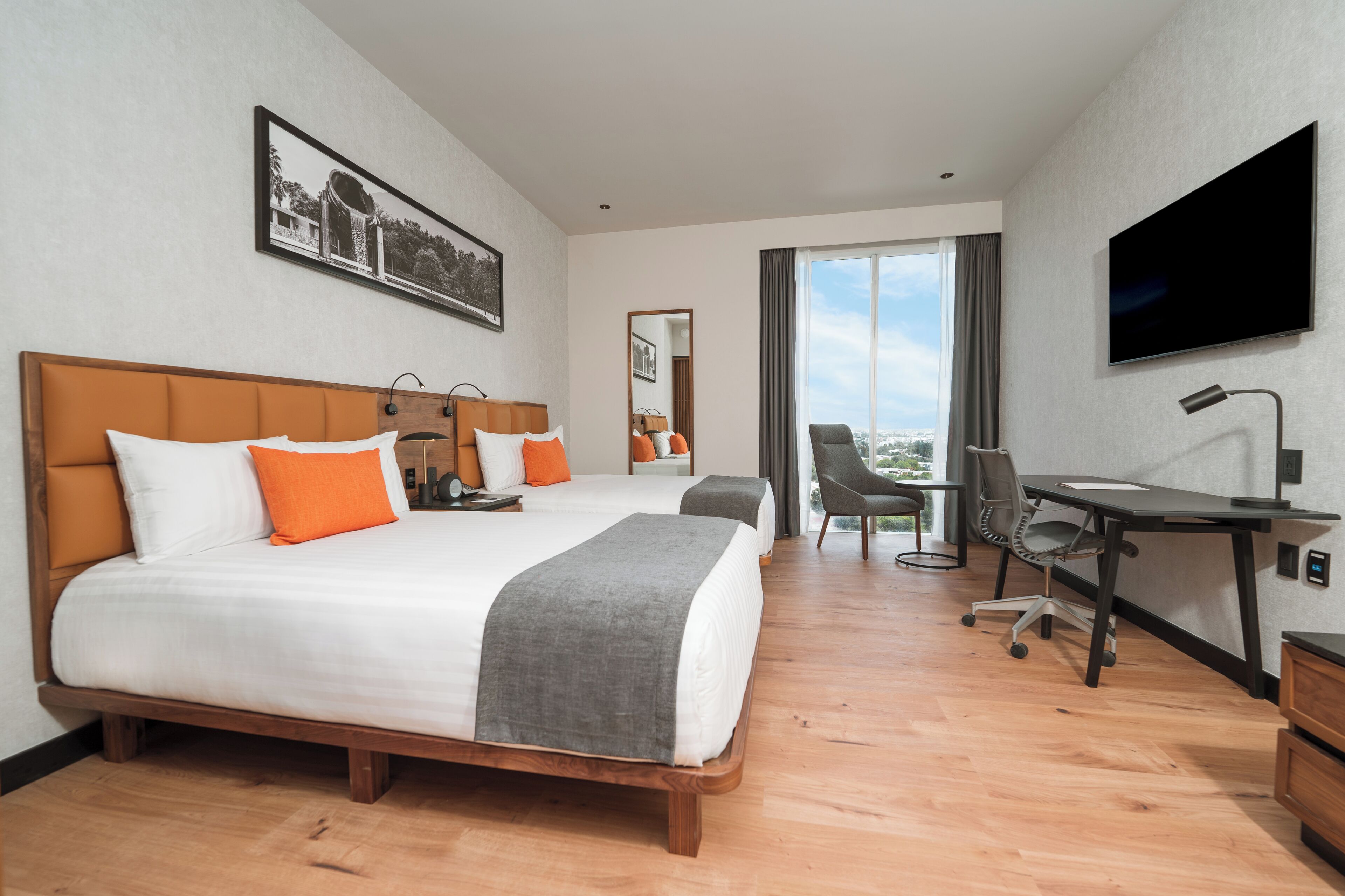 A hotel room with a large bed, a desk, a chair, a TV, and a window with a view.