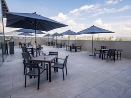 Un patio al aire libre con varias mesas y sillas, sombrillas grandes y vistas a la ciudad.