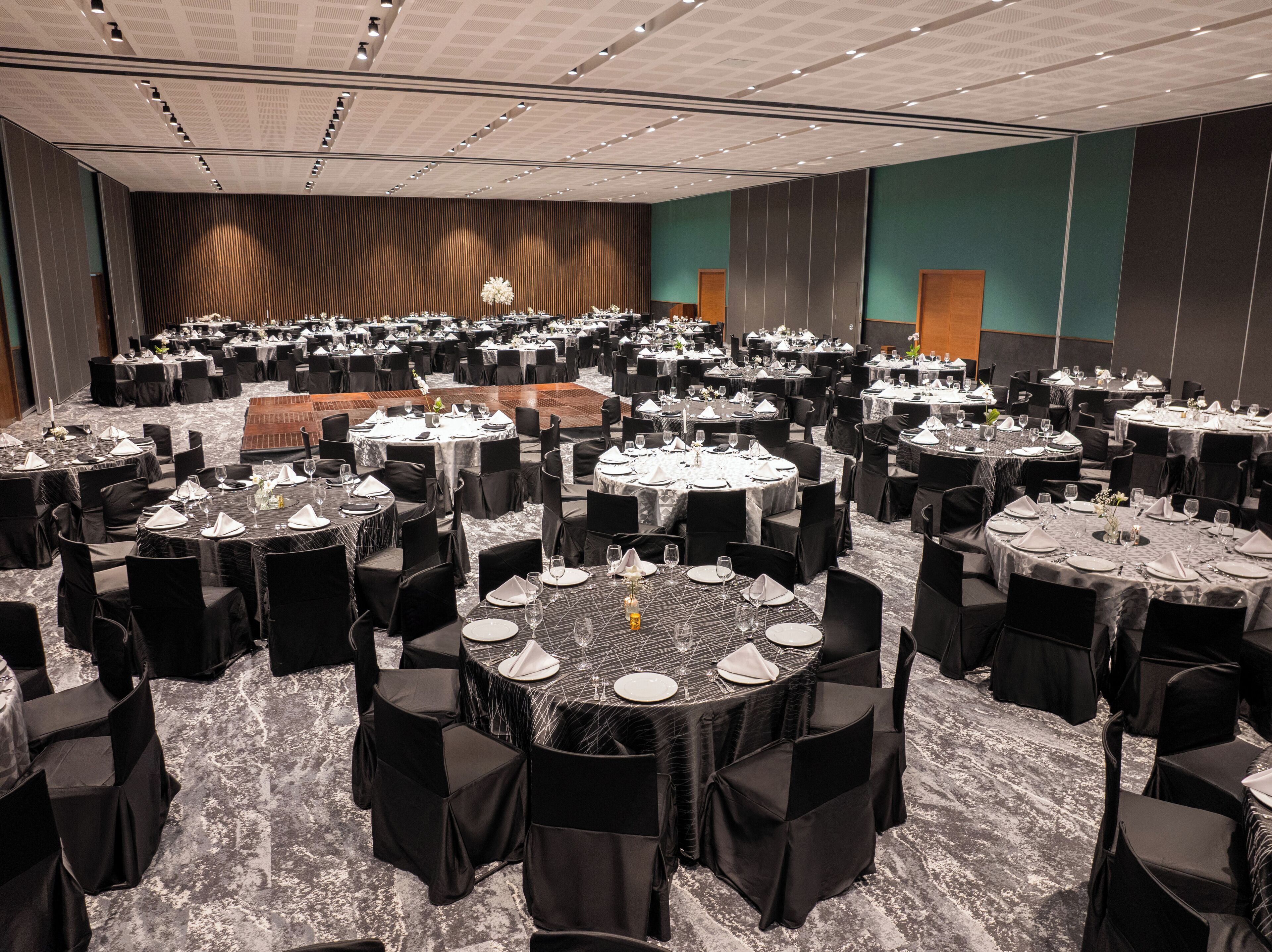 A large banquet hall with multiple round tables set for dining, each with chairs and table settings.
