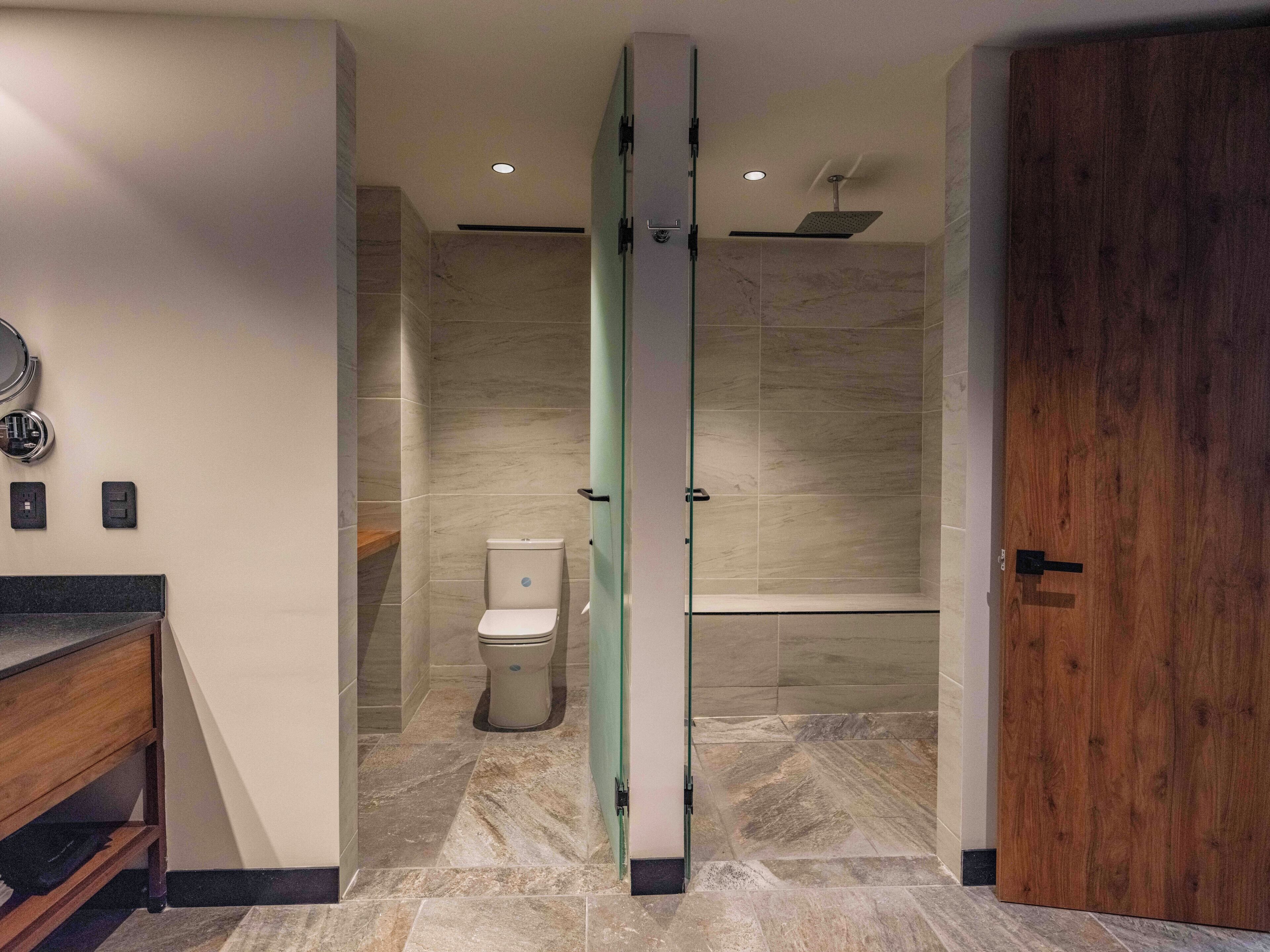 Un baño moderno con mampara de vidrio, inodoro, ducha y puerta de madera.