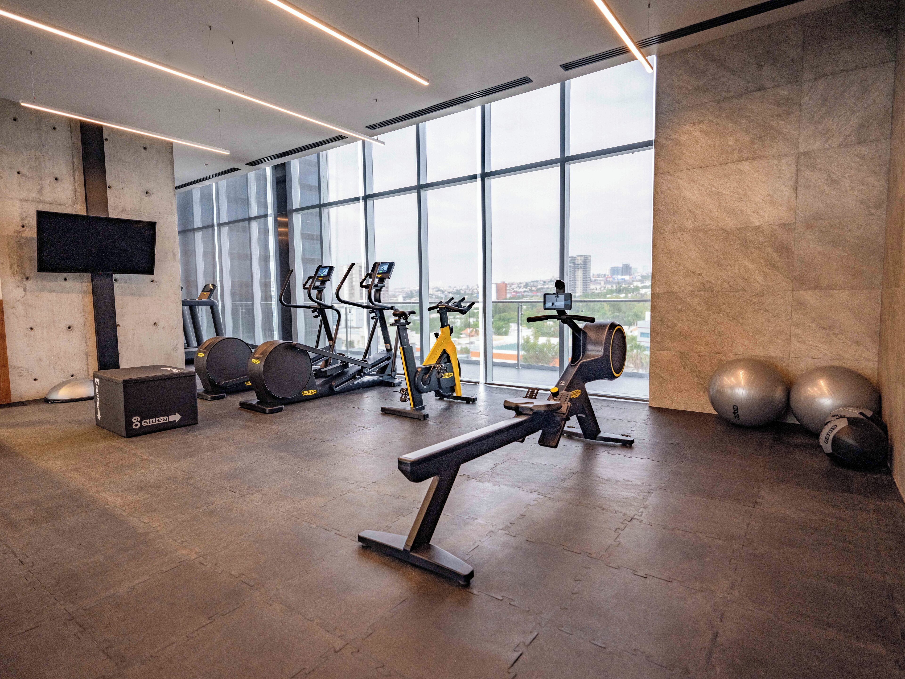 Un gimnasio moderno con equipo de ejercicio, ventanas amplias y vistas a la ciudad.
