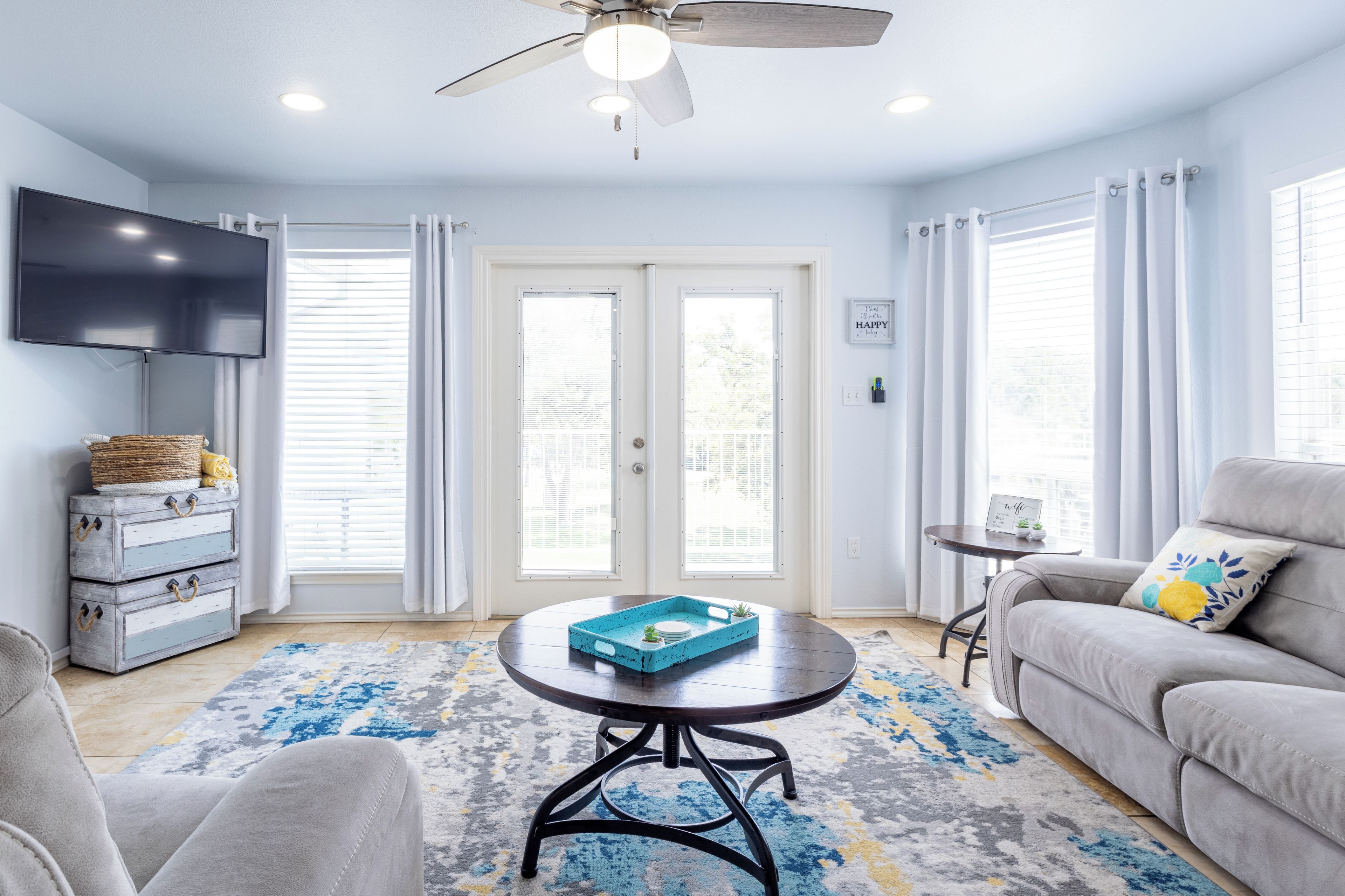 A living room with a ceiling fan, a flat-screen TV, a sofa, a coffee table, and a patterned rug.