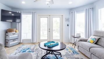 A living room with a ceiling fan, a flat-screen TV, a sofa, a coffee table, and a patterned rug.