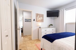 Un dormitorio con cama, escritorio, silla, televisor y puerta que da a otra habitación.
