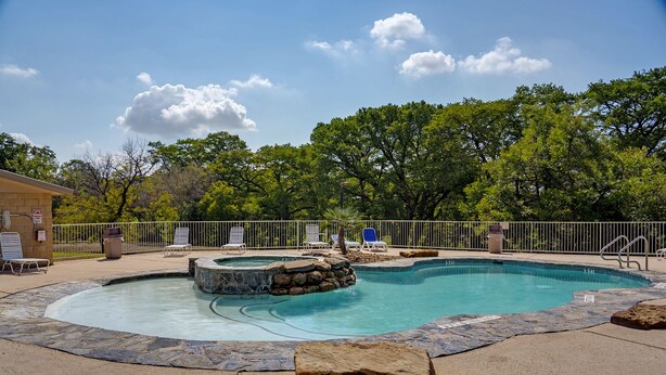 Una piscina con jacuzzi, rodeada de sillones de descanso y un borde de piedra.