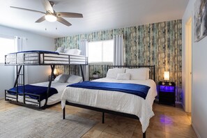 Une chambre avec des lits superposés, un ventilateur de plafond, une fenêtre avec des rideaux, une table de chevet avec une lampe et un mur orné d’un motif texturé.