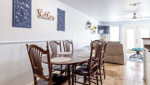 Un comedor con mesa y sillas de madera, un televisor montado en la pared y un ventilador de techo.