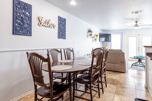 A dining area with a wooden table and chairs, a TV mounted on the wall, and a ceiling fan.