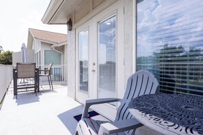 Een balkon met een tafel, stoelen, een schuifdeur en uitzicht op de lucht en bomen.