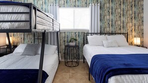 Una habitación con literas, una mesita redonda con una planta y una ventana con cortinas.