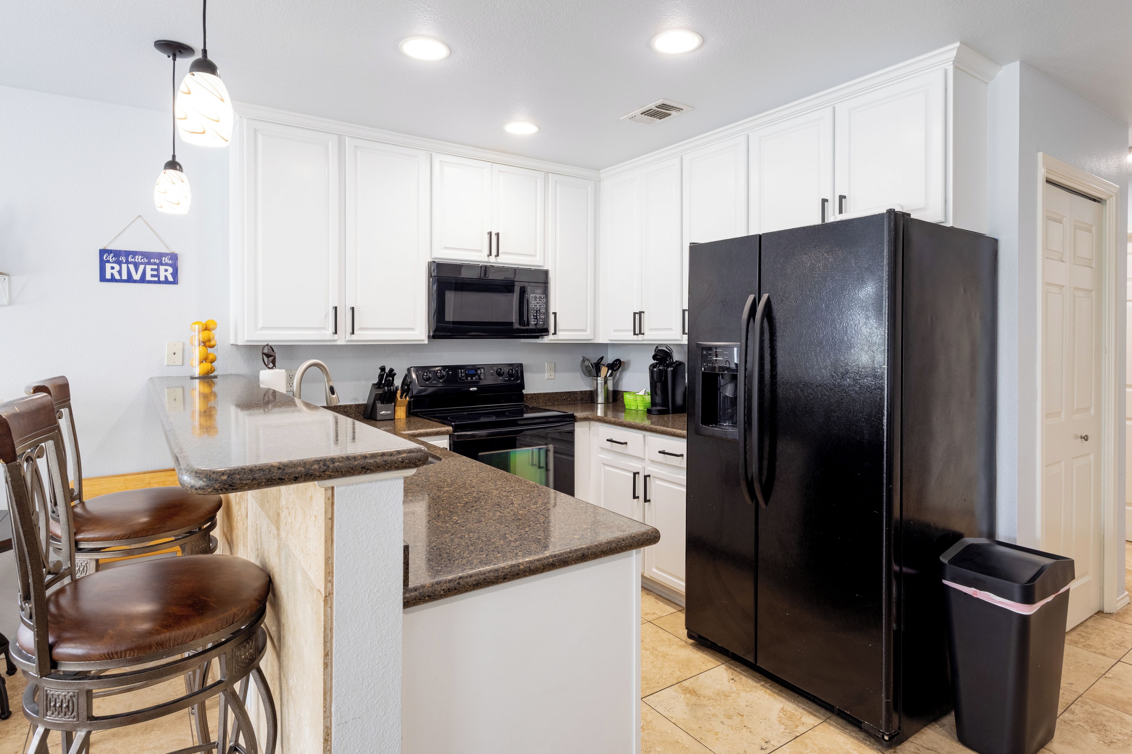 A modern kitchen with white cabinets, a black refrigerator, a microwave, and a bar area with stools.