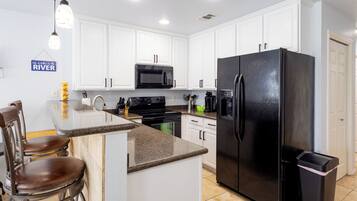 A modern kitchen with white cabinets, a black refrigerator, a microwave, and a bar area with stools.