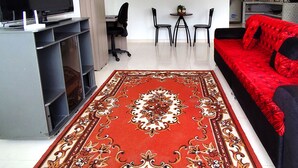 Un salon moderne avec un téléviseur à écran plat, un canapé rouge, une table basse et un tapis à motifs.
