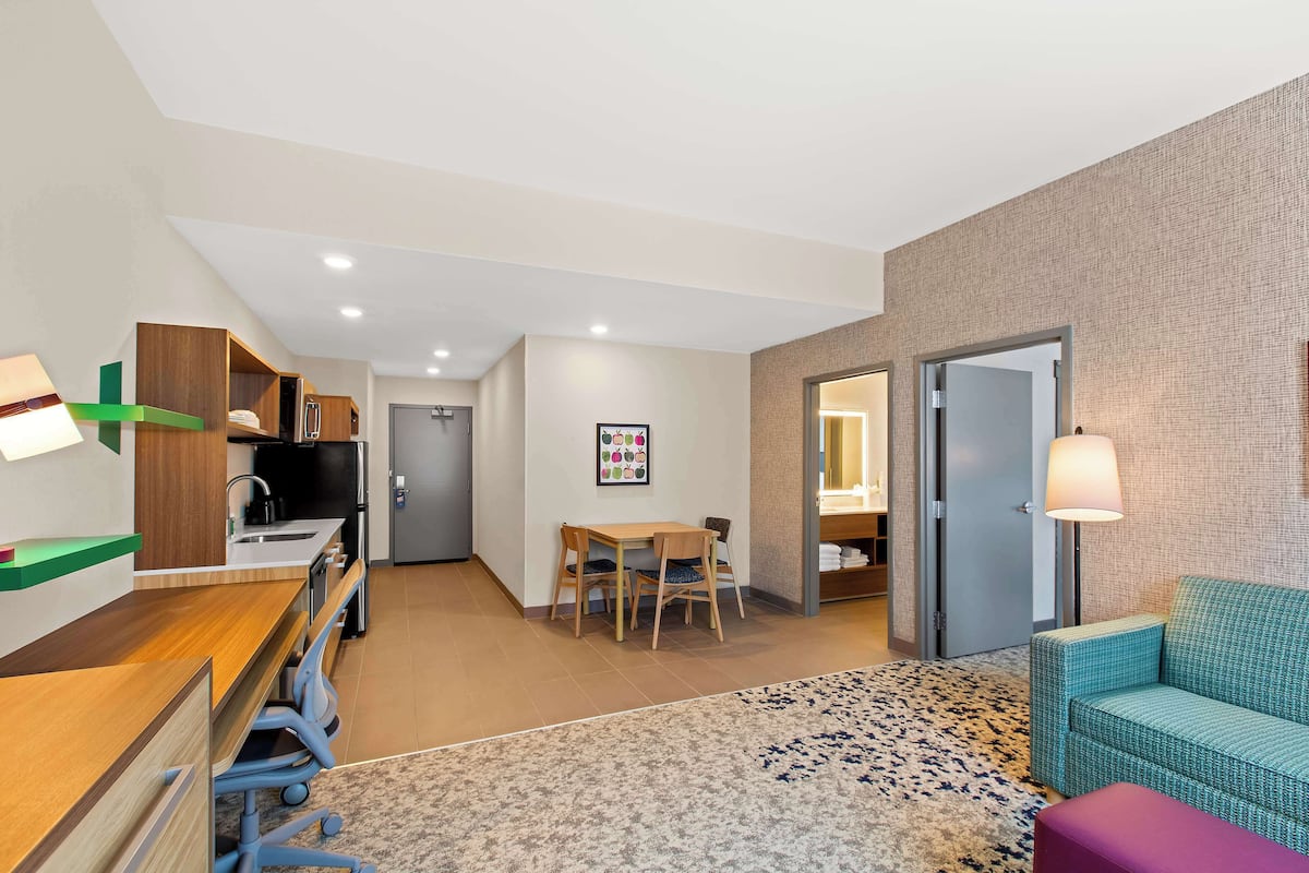 Habitación de hotel con kitchenette, comedor con mesa y sillas, sofá y alfombra estampada.