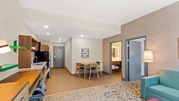 A hotel room with a kitchenette, a dining area with a table and chairs, a sofa, and a patterned rug.