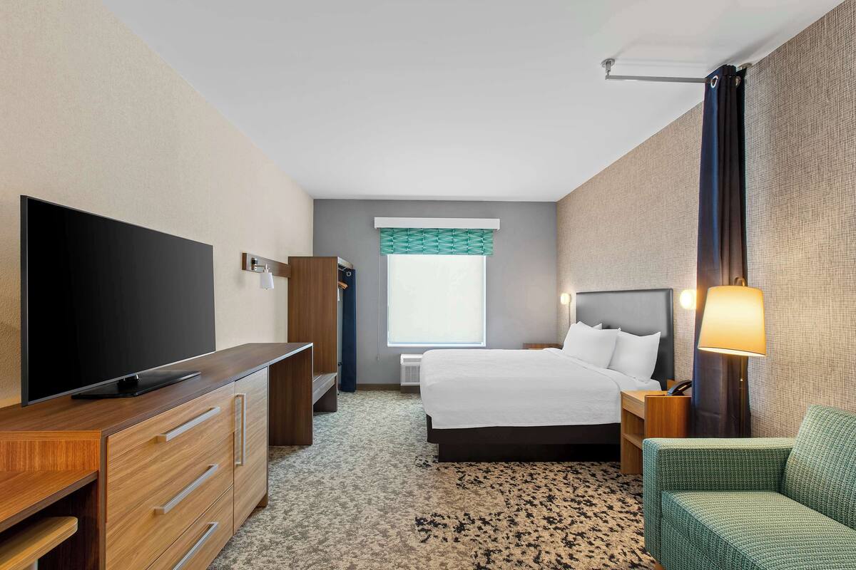 Habitación de hotel con cama, televisión, escritorio, silla y ventana con cortinas.