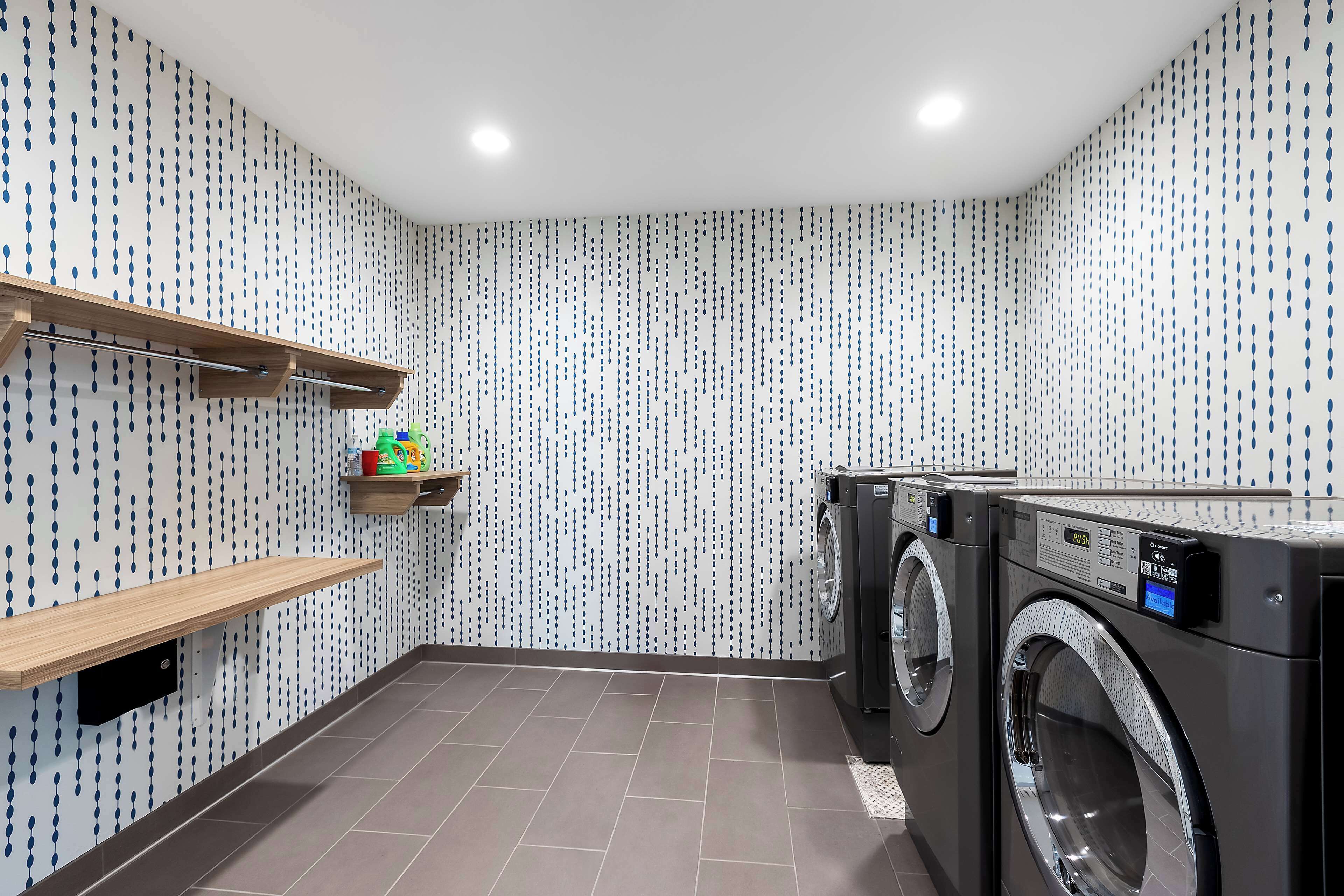 Une buanderie équipée de deux machines à laver, d’une étagère contenant des produits de lessive et d’un papier peint à motifs.