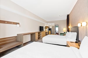 Una habitación de hotel con una cama, un escritorio, un televisor y un baño visible a través de una puerta abierta.