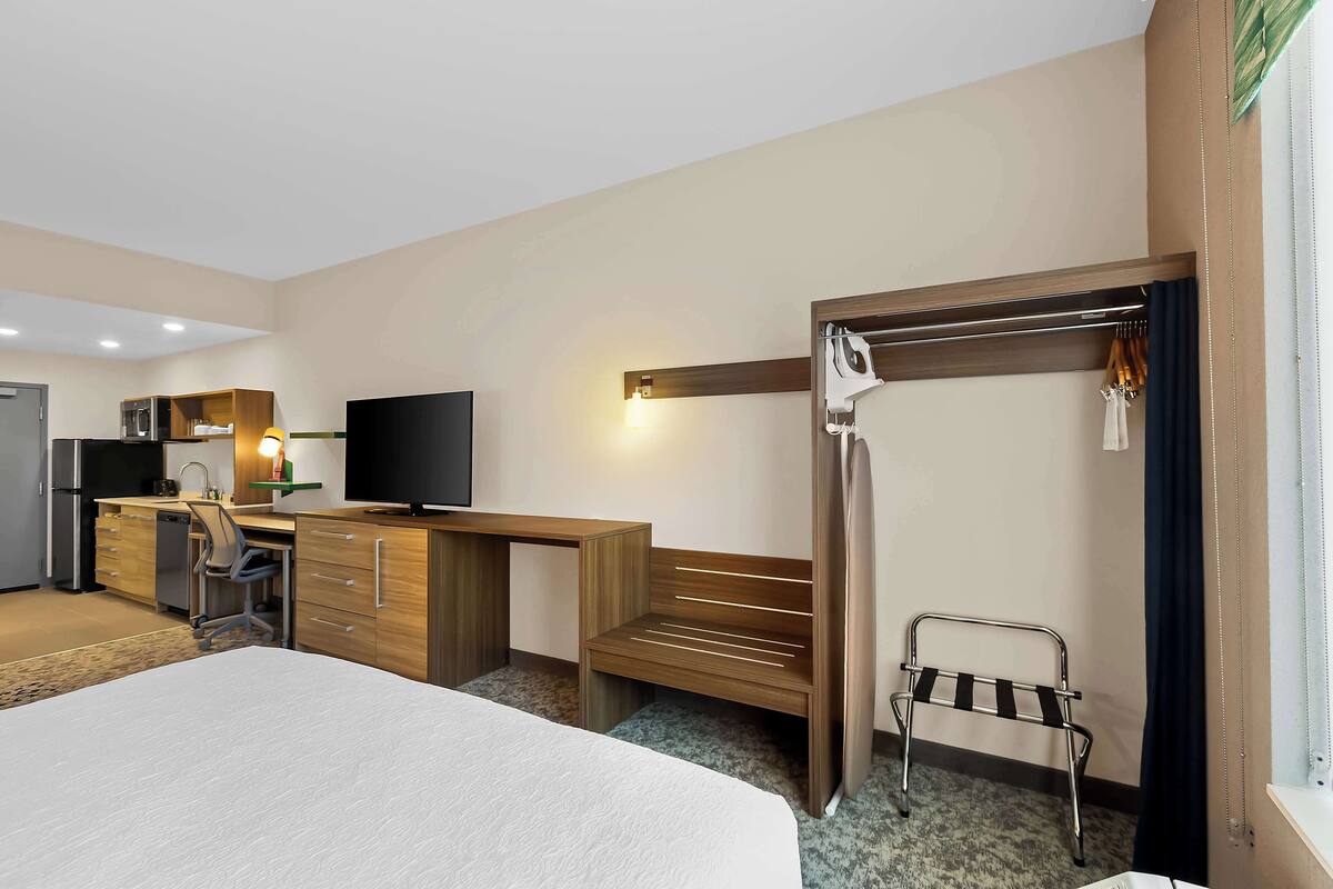 Habitación de hotel con cama, escritorio, silla, televisor, microondas y una pequeña kitchenette.