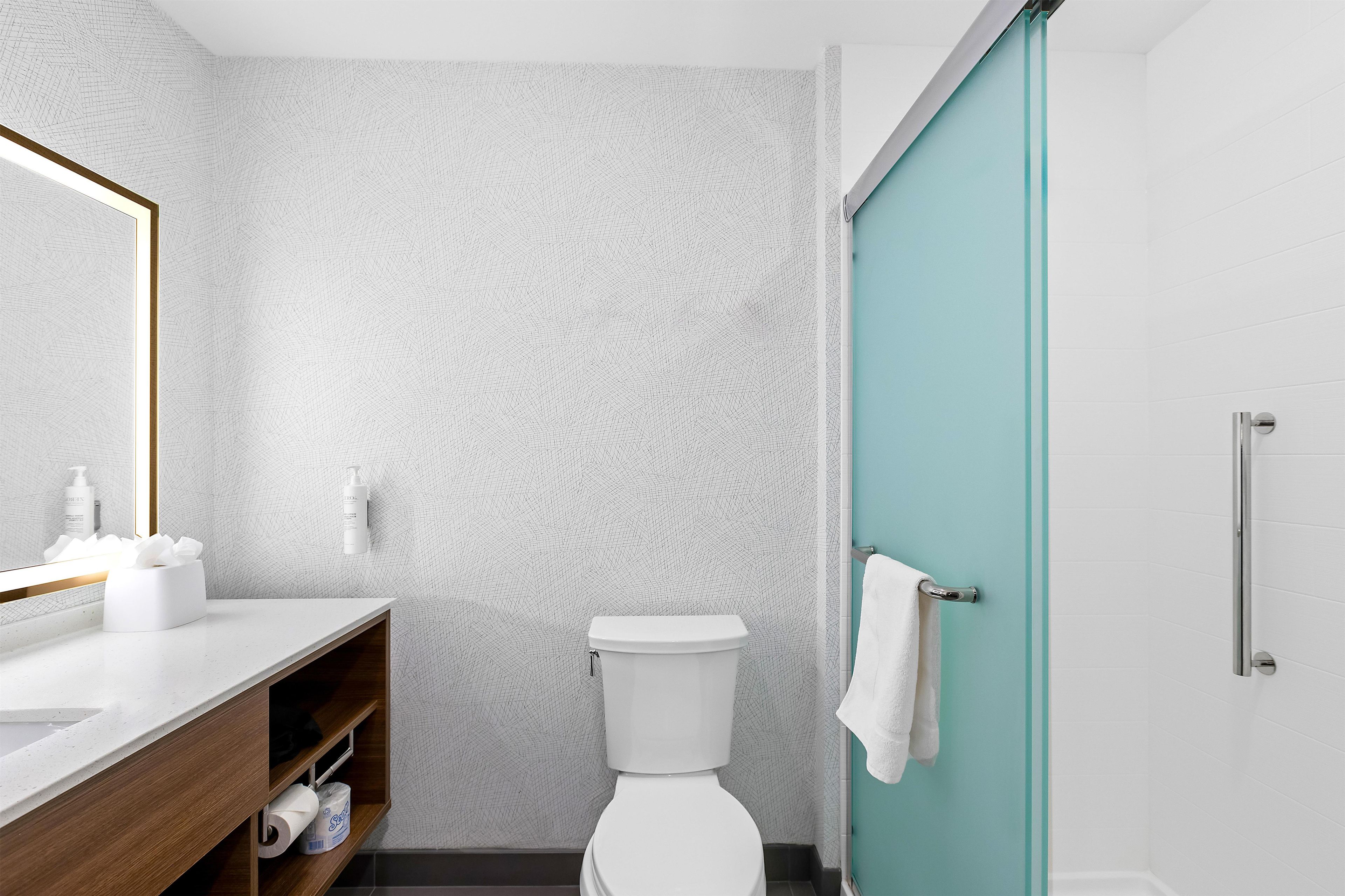 Une salle de bain avec un mur blanc à texture, un meuble-lavabo en bois, des toilettes blanches et une porte de douche turquoise.