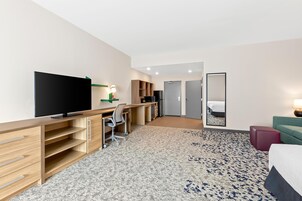 Quarto de hotel com televisão de tela plana, escrivaninha com cadeira, espelho grande, cama e um pequeno espaço de estar.