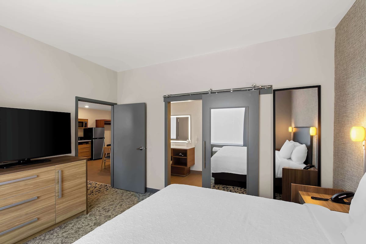 Habitación de hotel con cama, televisión, escritorio con teléfono y baño visible a través de una puerta abierta.