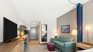 Quarto de hotel com cama, escrivaninha com televisão de tela plana, sofá verde, mesinha, espelho e abajur.