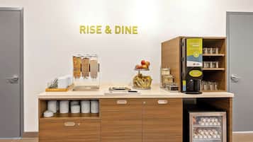 A breakfast station with a coffee machine, jars of condiments, and a fruit bowl.