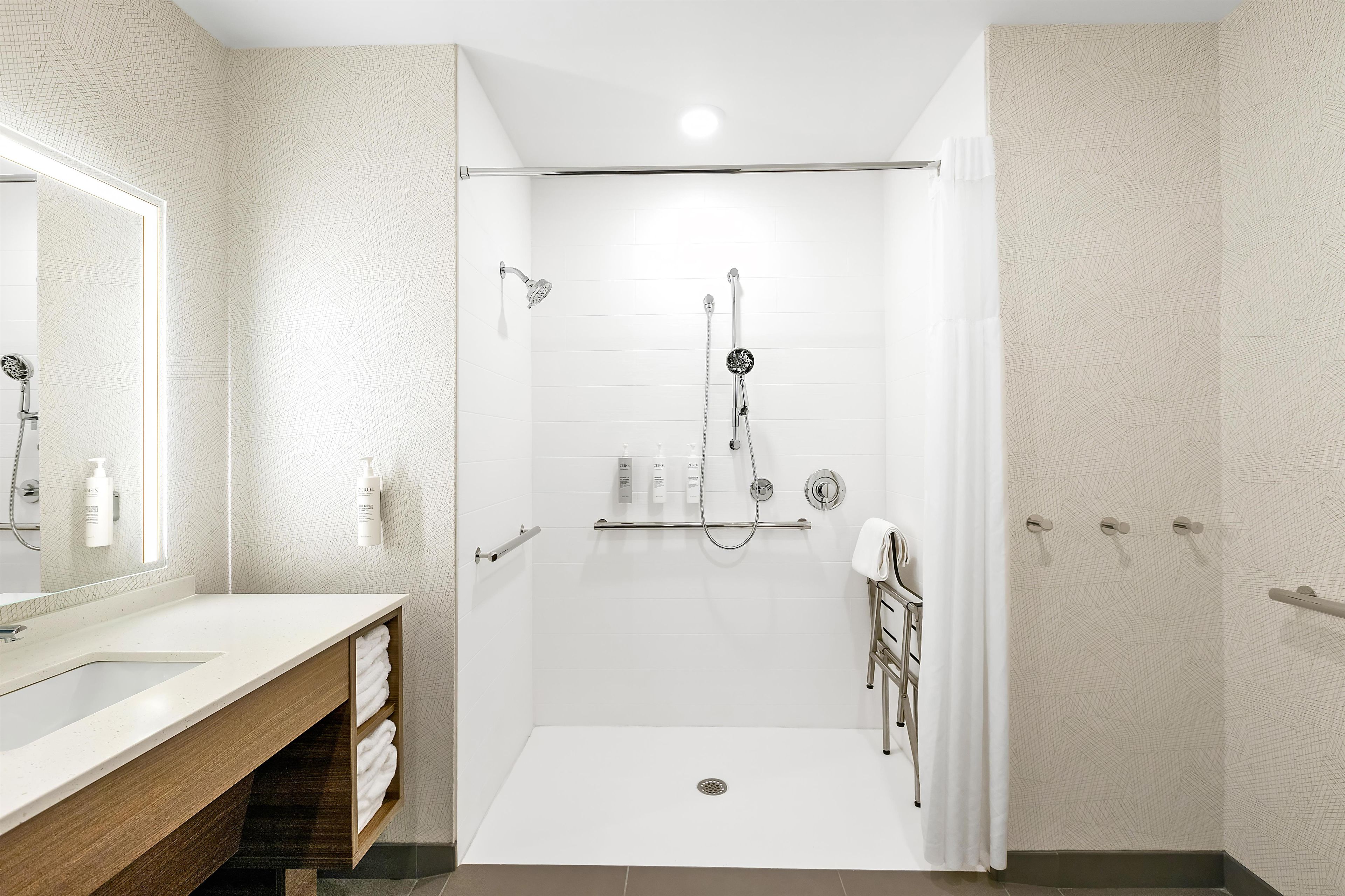 Un baño moderno con ducha a ras de suelo, tocador con espejo y un perchero para toallas.