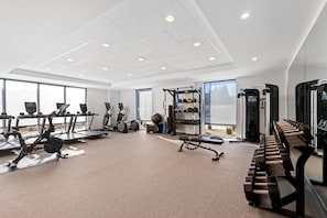 Une salle de sport moderne équipée de tapis de course, de vélos elliptiques, de poids libres et d’un support pour les exercices de squat.