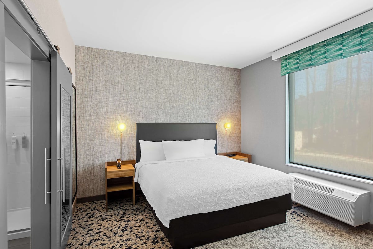 Una habitación de hotel moderna con una cama grande, lámparas de noche, un calentador y un ventanal con persianas.