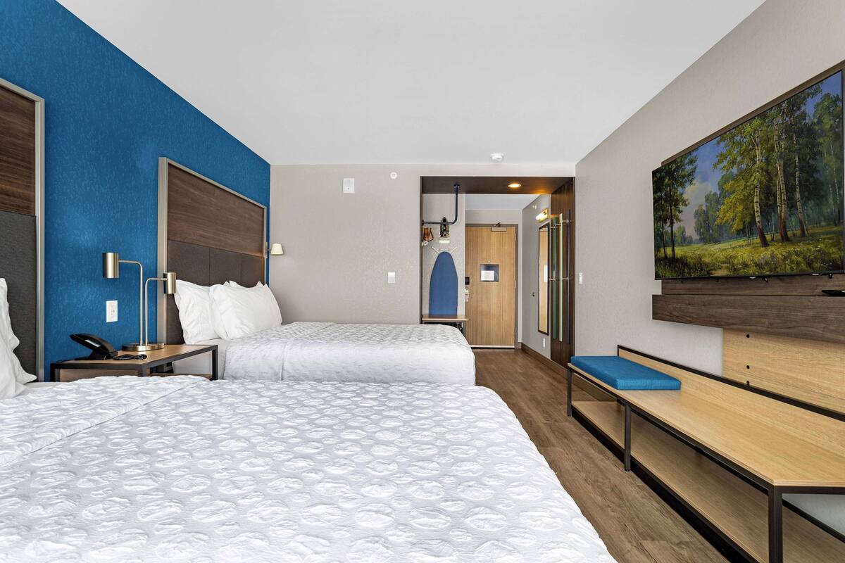 Une chambre d’hôtel avec deux lits, un bureau, une chaise, une télévision et un tableau au mur.