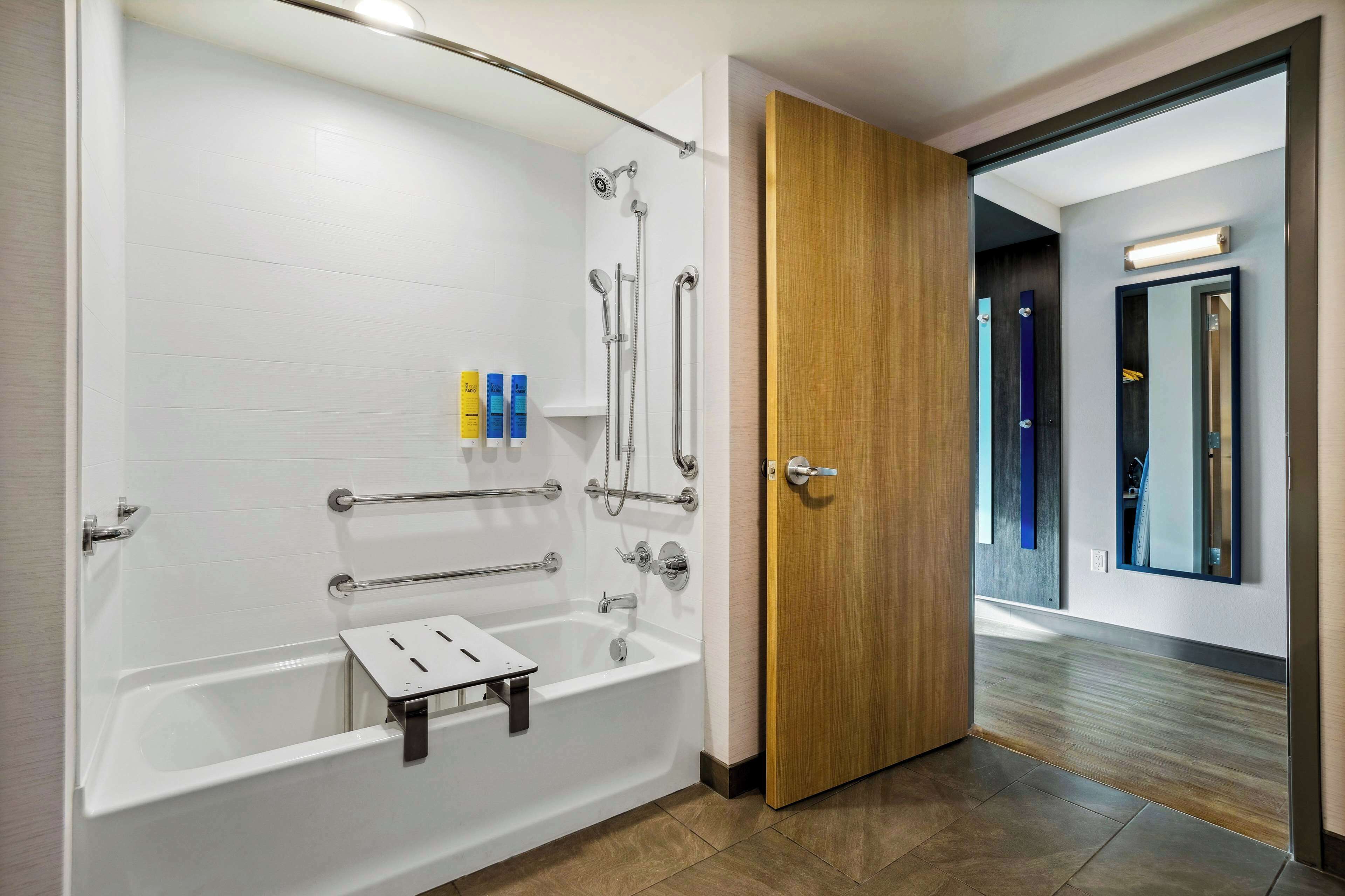 A modern bathroom with a walk-in shower, grab bars, and a wooden door.