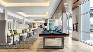 Un área interior de piscina moderna con mesa de billar, asientos y ventanas amplias.