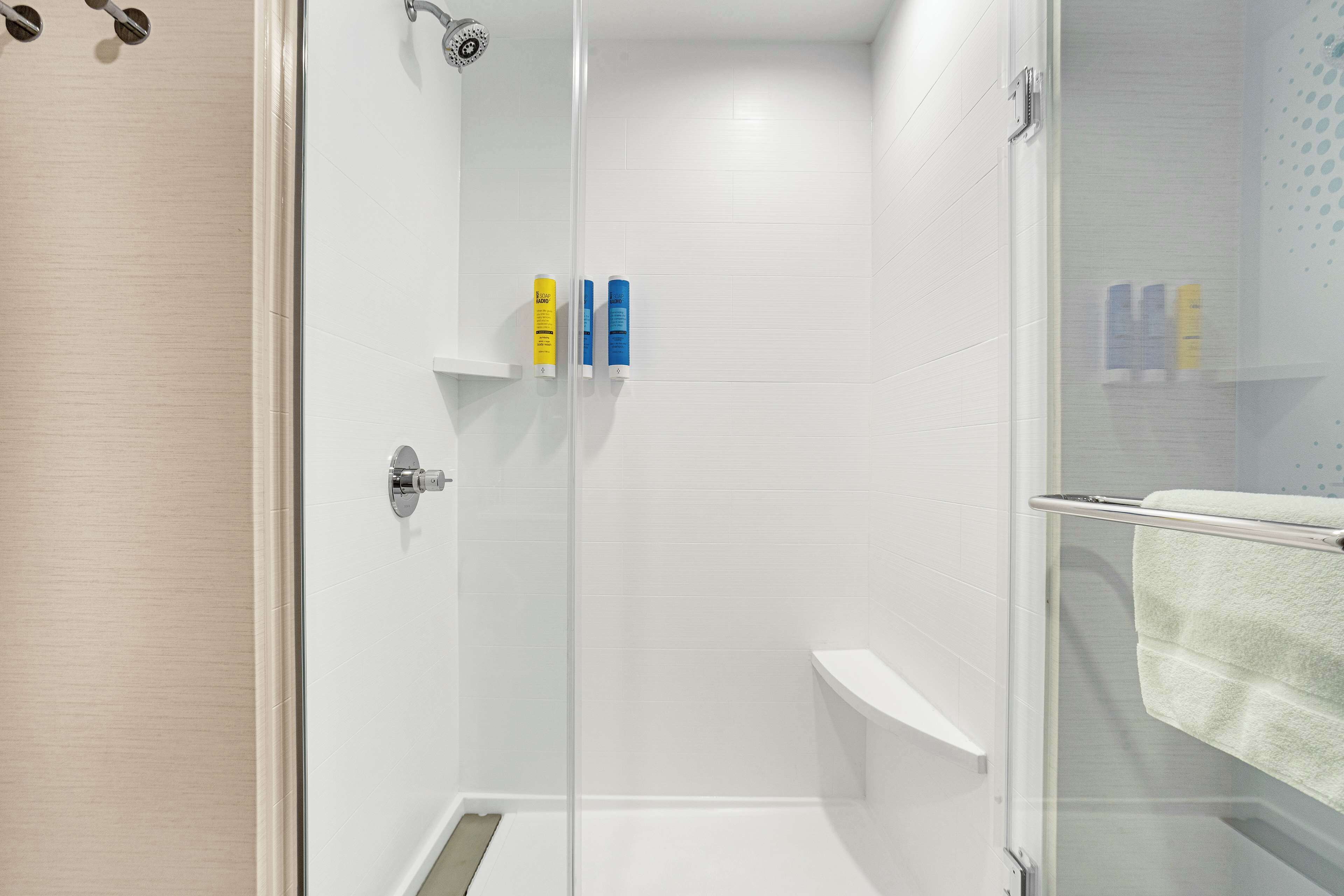 Un área de ducha moderna con puerta de cristal, paredes de azulejos blancos y un perchero para toallas.