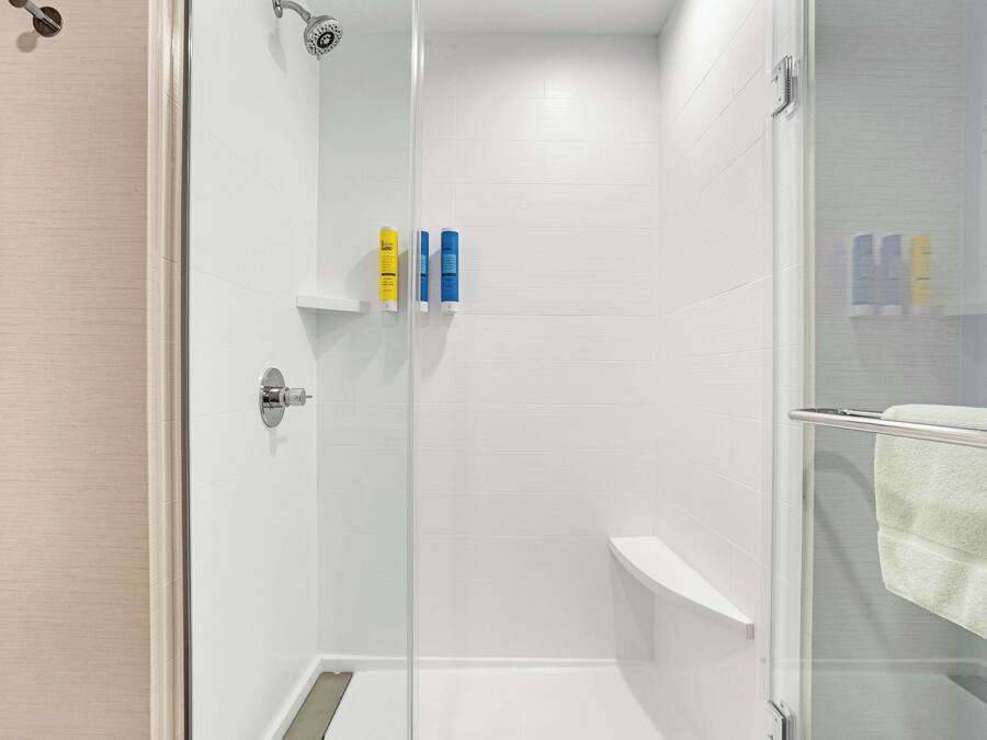 Un área de ducha moderna con puerta de cristal, paredes de azulejos blancos y un perchero para toallas.