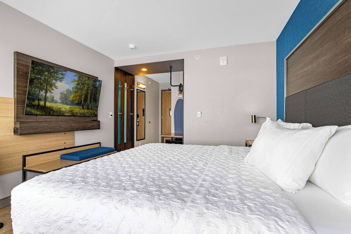 Une chambre d’hôtel moderne avec un grand lit, un tableau au mur et une vue sur le couloir.