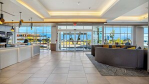 Un moderno vestíbulo de hotel con una recepción, zona de estar y ventanas amplias que ofrecen vistas al exterior.