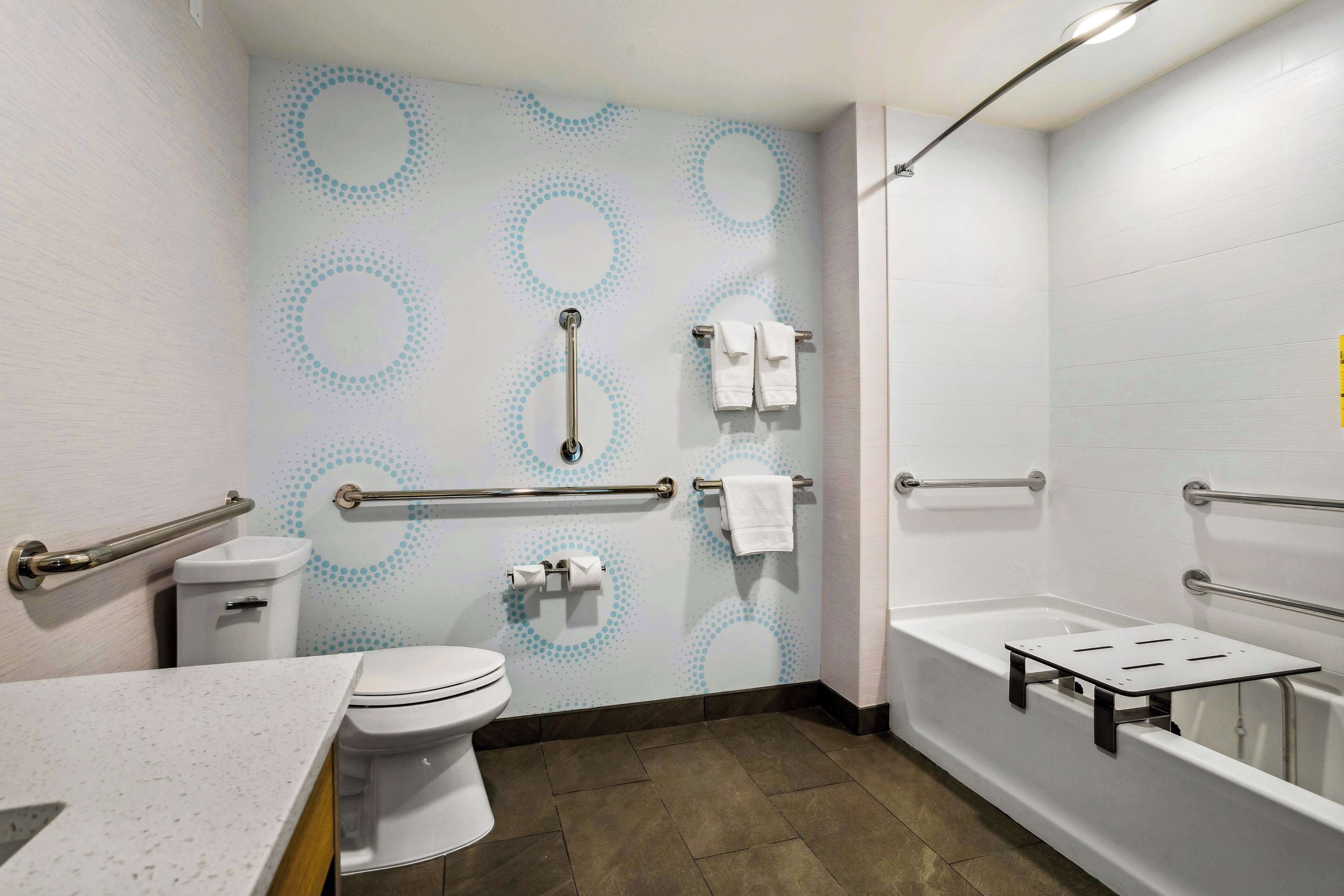 A bathroom with a toilet, sink, and bathtub. It includes grab bars and a handrail for accessibility.