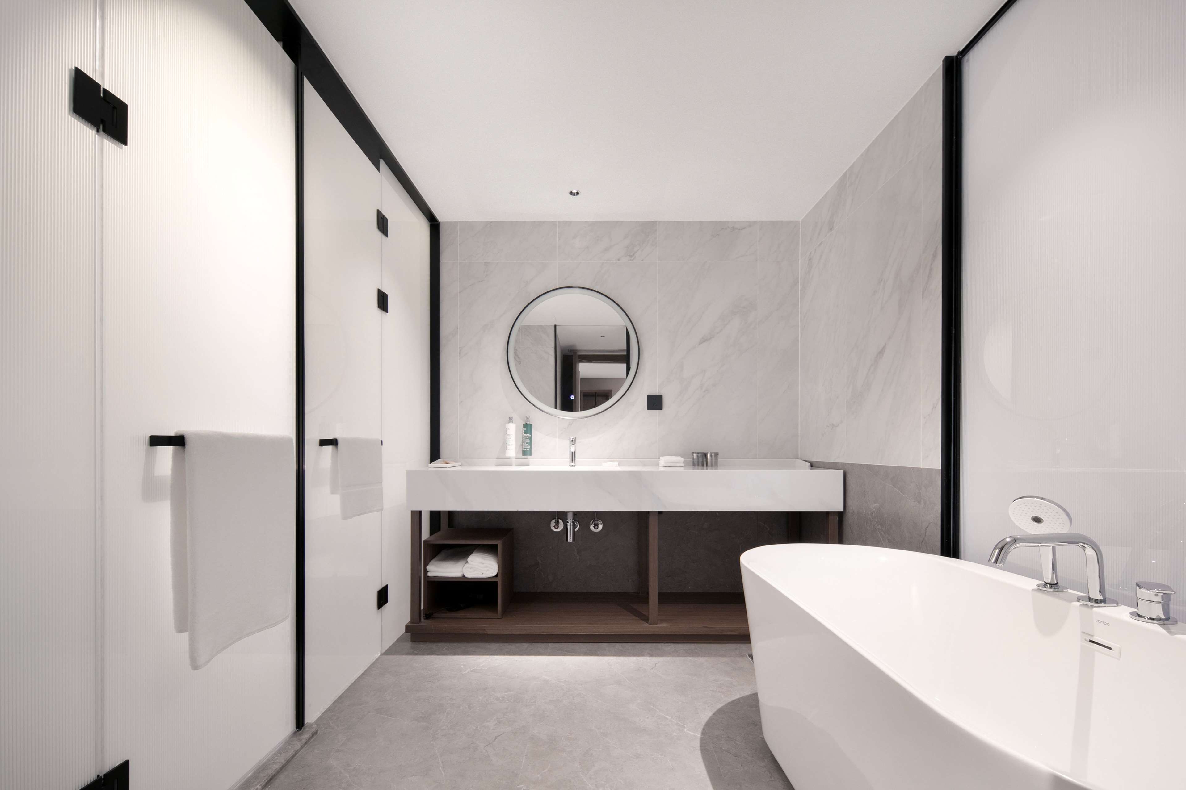 A modern bathroom with a freestanding bathtub, a round mirror above the sink, and a towel rack.