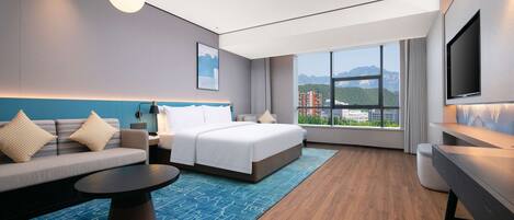 Una habitación de hotel moderna con cama, sofá, escritorio y ventana grande con vistas a la ciudad.