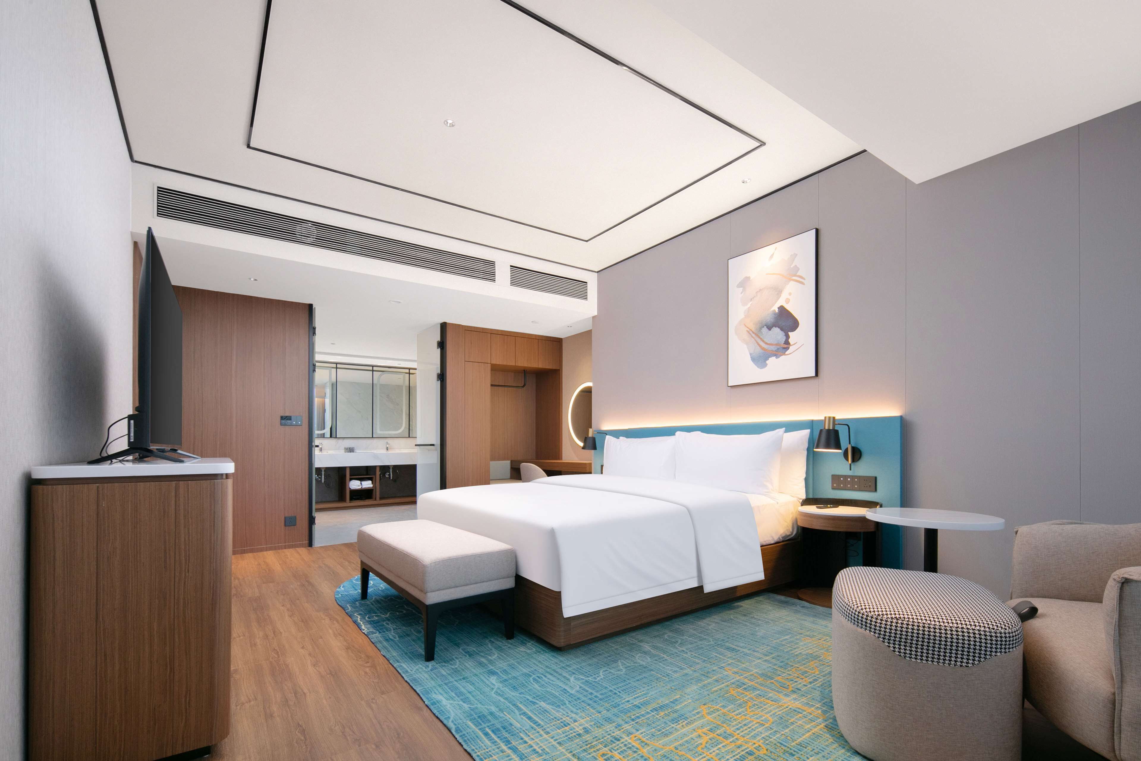 Een moderne hotelkamer met een groot bed, een bureau, een stoel en een klein voetenbankje.