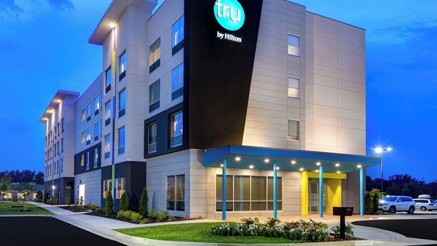 Un hôtel moderne, reconnaissable à son enseigne « tru by Hilton » bien visible, avec de nombreux étages et une entrée bien éclairée.