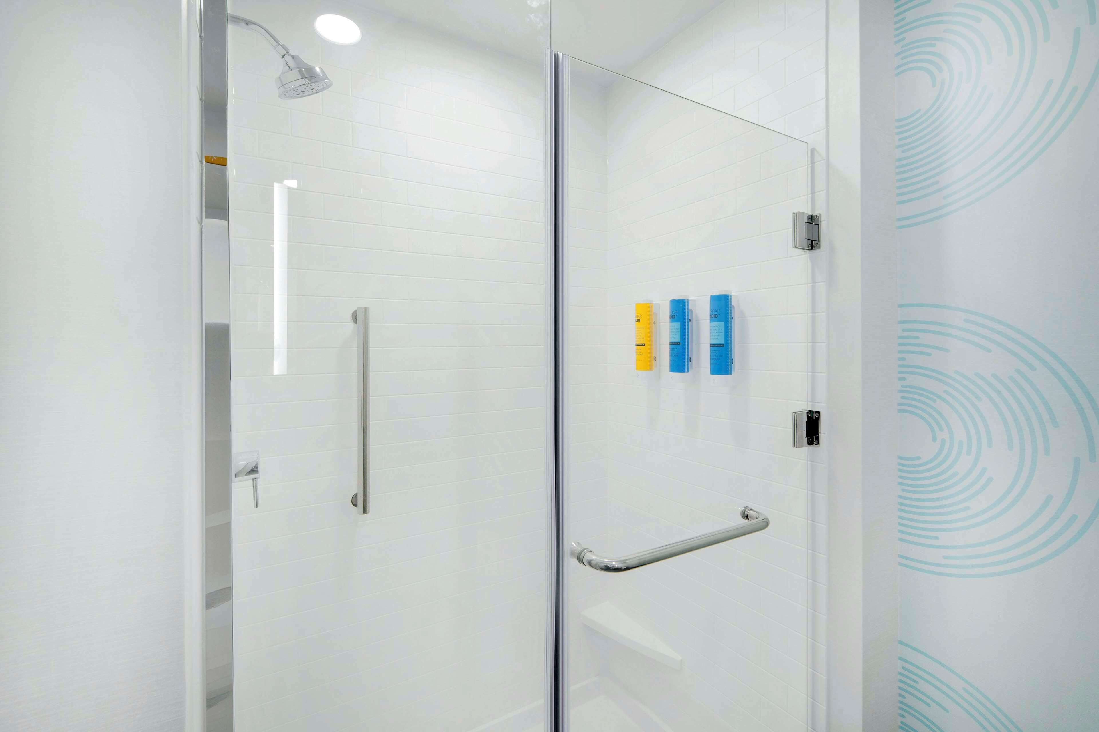A modern bathroom with a glass shower enclosure, a white tiled wall, and a handrail.