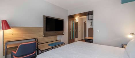 Habitación de hotel con cama, escritorio con silla, televisor montado en la pared y baño visible a través de una puerta abierta.